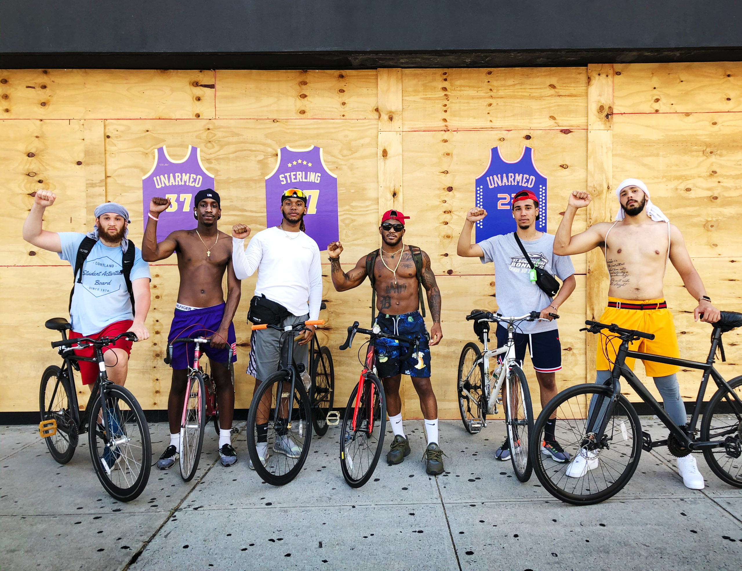 Six Black Men Standing in Front of “Unarmed” Prints, by Raafi Rivero